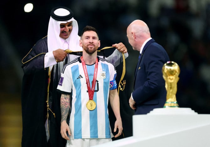 Qatar's Emir Sheikh Tamim bin Hamad Al-Thani wraps a robe around Lionel Messi on stage next to the FIFA World Cup trophy after Argentina won the Qatar 2022 World Cup final. (Reuters)