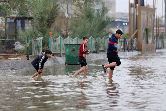Iraqi children cross a flooded street in the Iraqi capital Baghdad after heavy rains, on Dec. 24, 2022. (AFP)