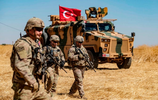 US troops walk past a Turkish military vehicle during a joint patrol with Turkish troops in the Syrian village of al-Hashisha on the outskirts of Tal Abyad town along the border with Turkish troops. (AFP file photo)