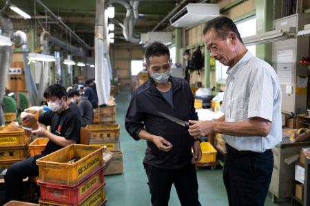 This picture taken on September 2, 2022, shows Katsumi Sumikama (right), head of Sumikama Cutlery, checking the quality of a knife at his factory in Seki, Gifu prefecture. (AFP)