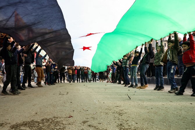 Children unfurl a giant Syrian opposition flag during a rally in Idlib on Jan. 6, 2023 against a potential rapprochement between Turkiye and the Syrian regime. (AFP)