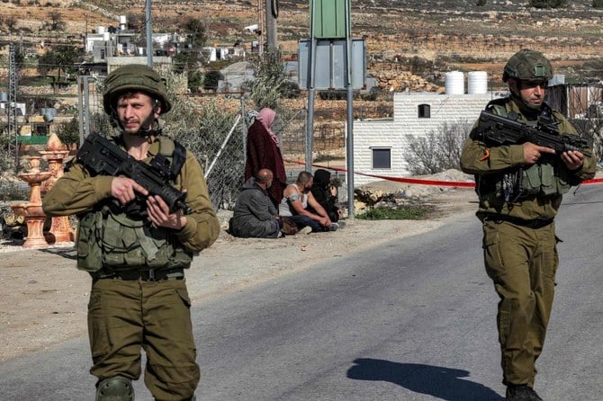 Eyewtinesses who were in a nearby vehicle stand on the side of a road by Israeli soldiers at the scene near the body of Palestinian Hamdi Abu Dayyeh in the village of Halhul north of the city of Hebron in the occupied West Bank. (AFP)