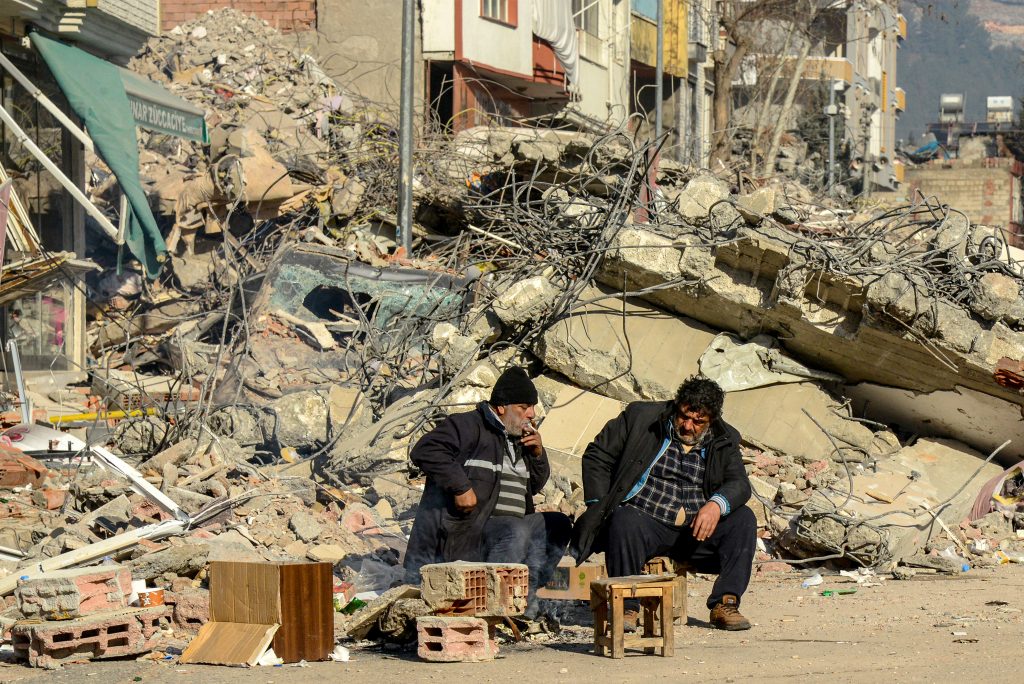 Victims' relatives sit next to the rubble of a collapsed building in Adiyaman, Turkey on February 9, 2023, three days after a 7,8-magnitude earthquake struck southeast Turkiye. (AFP)