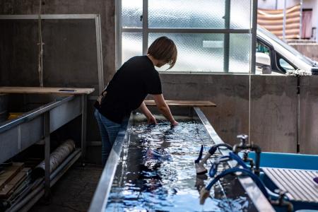 This picture taken on August 22, 2022 shows an employee of artisan Toma Chinen, who inherited the workshop of one of three Bingata-making families that once served Ryukyu royalty, washing off the starch from material in Naha, in Japan's Okinawa Prefecture. (AFP)