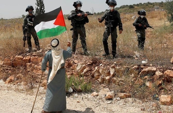 A demonstrator holds a Palestinian flag facing Israeli forces near Tulkarm in June 2020. Israel, which collects taxes on behalf of the Palestinian Authority, would use $29m from PA funds to compensate victims of Palestinian attacks. (Reuters/File)