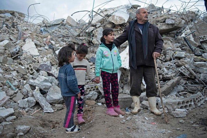 A family stands amidst the rubble of a collapsed building in the town of Jableh in Syria’s northwestern province of Latakia on February 7, 2023 following a deadly quake. (AFP)