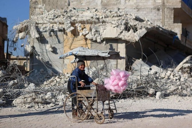 A Syrian child selling cotton candy smiles as he stands in front of the rubble of a collapsed building following last week's earthquake in Syria's rebel-held village of Atarib, in Aleppo province, on February 14, 2023. (AFP)