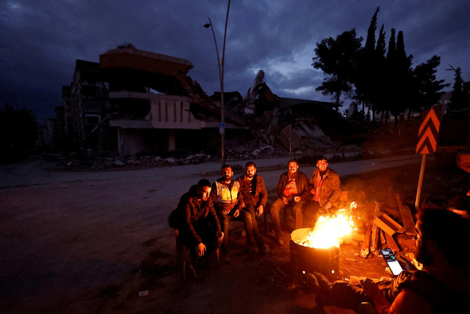 People warm themselves by a fire beside a collapsed building and rubble, in the aftermath of a deadly earthquake, in Antakya, Hatay province, Turkiye, Feb. 21, 2023. (Reuters)