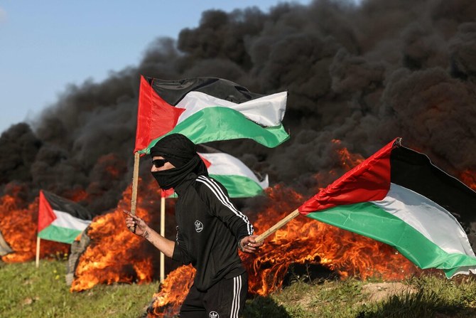 A Palestinian youth waves national flags as other burn tires, during a protest near the Israel-Gaza border east of Gaza City, on February 22, 2023. (AFP)