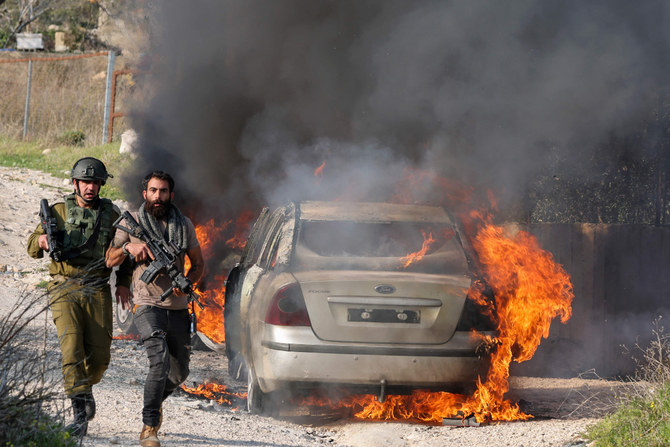 A member of Israeli security forces and one from settlement security walk past a burning car reportedly set on fire by settlers in the Palestinian Burin village on Feb. 25, 2023. (Jaafar Ashtiyeh / AFP)