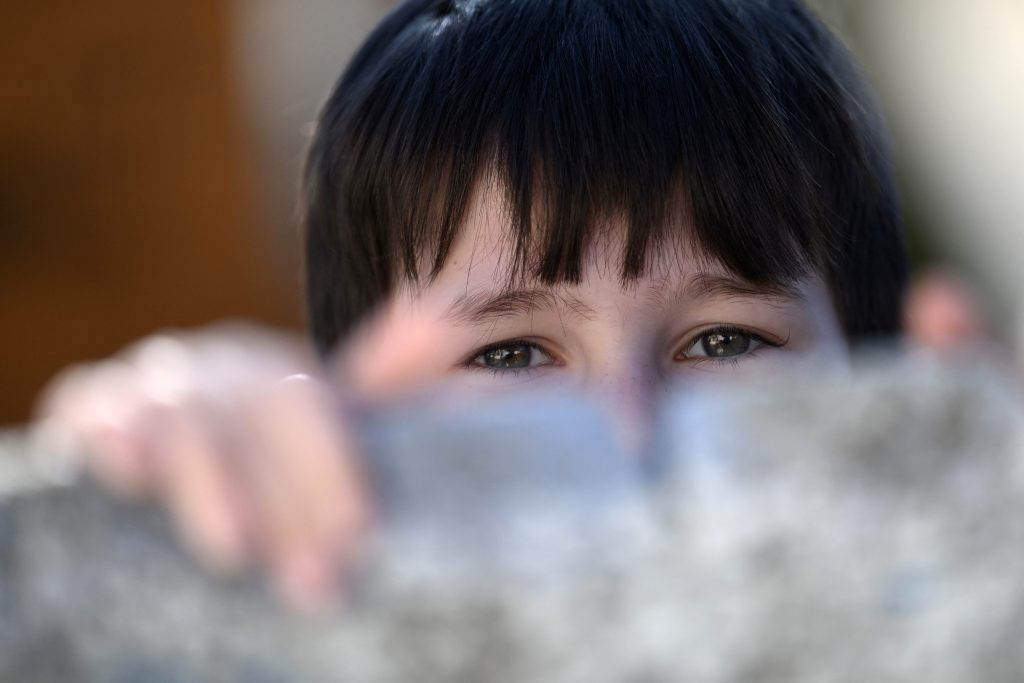 A refugee boy looks over a barrier at the refugee shelter, where currently around 150 Roma and Ukrainians live together, in Uzhhorod, western Ukraine, on March 2, 2023. (AFP)