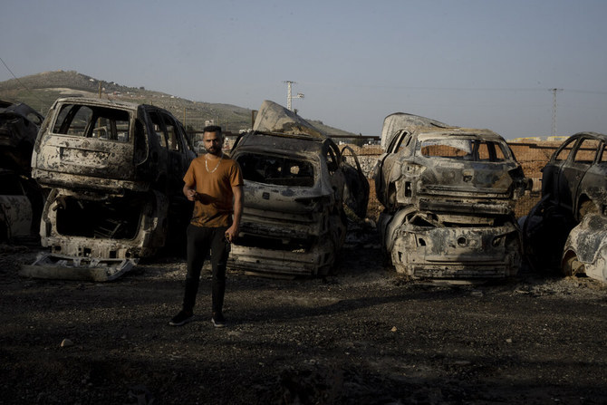 A Palestinian man smokes as he stands among vehicles torched in a rampage by settlers in Hawara, near the West Bank city of Nablus, Tuesday, Feb. 28, 2023. (AP)
