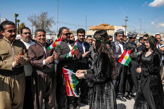 Women hand out small Kurdistan flags to men gathering in Arbil on March 11, 2023, during a commemoration marking the 32nd anniversary of an uprising against the regime of toppled dictator Saddam Hussein. (AFP)