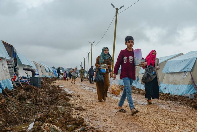 People carry food on a muddy path next to tents donated by Turkish Turk Kizilay humanitarian organization, following floods in southeastern Turkey. (File/AFP)
