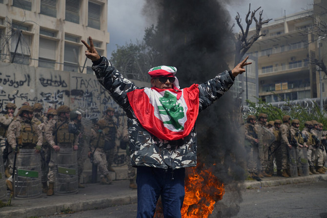 A retired soldier wearing a Lebanese flag, flashes the victory sign as Lebanese army soldiers stand guard during a protest demanding better pay and living conditions in front of the Lebanese Central Bank in Beirut on Mar. 30, 2023. (AP)