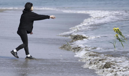 A man throws flower to the sea in tribute to the victims in the 2011 earthquake and tsunami in Arahama area, Sendai city, northern Japan, on Saturday, March 11, 2023. (Kyodo News via AP)