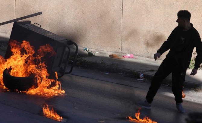 A Palestinian throws a tire onto a fire, creating a roadblock, during a raid by Israeli soldiers in the city of Nablus in the occupied West Bank on April 3, 2023. (AFP)