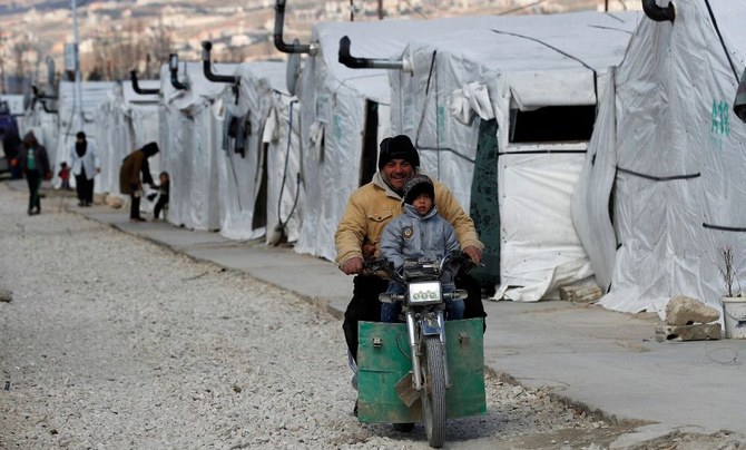 A displaced Syrian man and his son ride a motorcycle, as they drive between the tents at a refugee camp, in Bar Elias, in eastern Lebanon’s Bekaa Valley, March 5, 2021. (AP Photo)