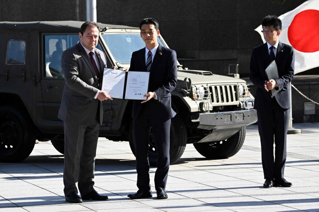 Japan's State Minister of Defence Toshiro Ino (C) and Ukrainian Ambassador to Japan Sergiy Korsunsky (L) pose with a list of Japanese Self-Defense Force vehicles that were handed over to Ukraine, during a ceremony at the Defence Ministry in Tokyo on May 24, 2023. (Photo by Kazuhiro NOGI / AFP)