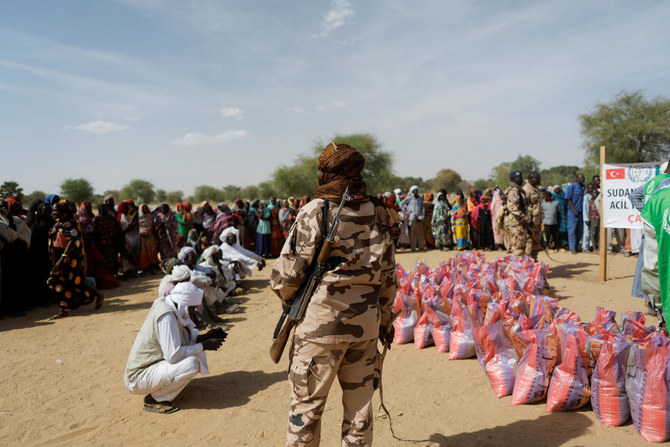A soldier stands as Sudanese women who fled the violence in their country, wait to receive food supplies from a Turkish aid group near the border between Sudan and Chad. (Reuters)