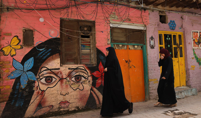 Iraqi women walk past art work painted on houses in Baghdad’s Al-Anbari neighbourhood on April 10, 2023. (AFP)