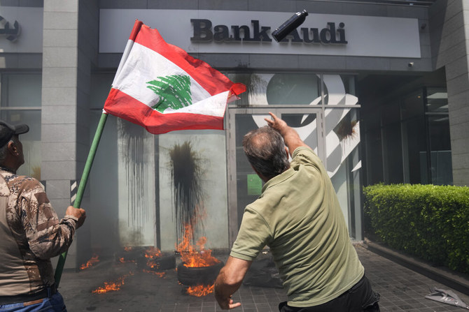 A protester throws a bottle of oil at the windows of Bank Audi during a protest demanding the release of depositors’ trapped savings, in Beirut, on June 15, 2023. (AP)