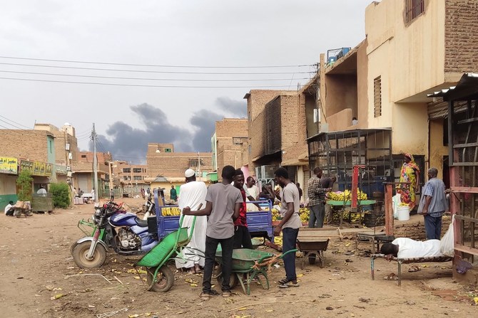 Smoke rises above buildings as people gather at a market to buy food provisions, in Khartoum on June 10, 2023. (AFP)