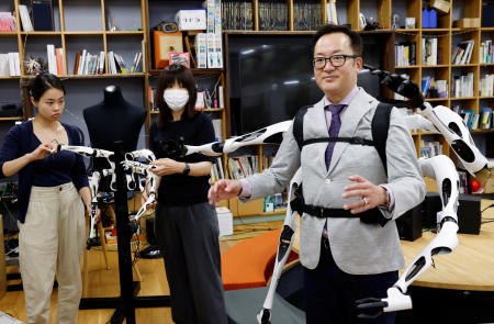 Staff members control the robot arm control unit which is synced with wearable robot arms 