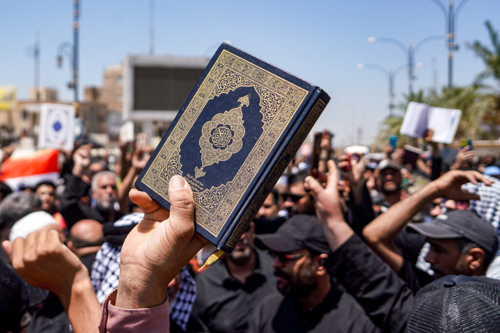 A demonstrator holds a copy of the Quran, Islam's holy book, during a rally after the weekly Friday prayers denouncing the burning of the Quran in Sweden in Iraq's central shrine city of Kufa east of nearby Najaf on July 21, 2023. (AFP)