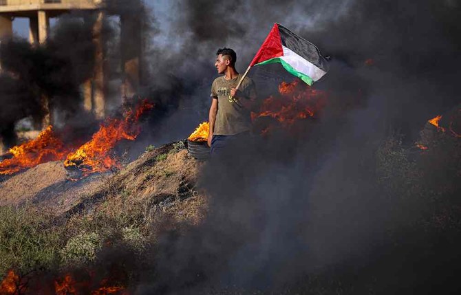 A Palestinian youth holds a flag next to burning tyres during a protest by the border fence with Israel east of Gaza City on on July 3, 2023. Israel has stepped up operations in the northern West Bank, home to Jenin city and its adjacent refugee camp. (AFP)