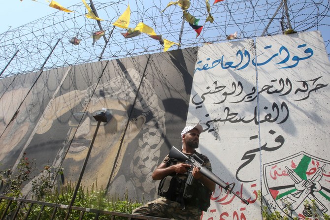 File photo of A gunman, belonging to Palestinian president Mahmud Abbas's Fatah movement, stands guard next to a graffiti of late leader Yasser Arafat in Ain el-Helweh camp, Lebanon's largest Palestinian refugee camp, near the southern coastal city of Sidon (AFP)