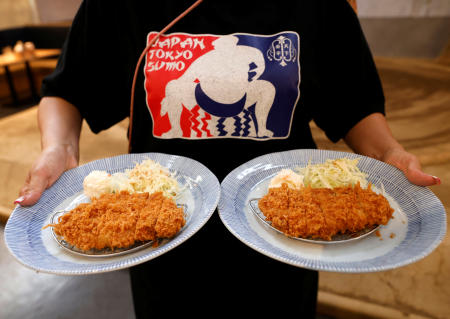 An employee of Yokozuna Tonkatsu Dosukoi Tanaka, a sumo wrestling themed restaurant, serves Tonkatsu or breaded pork cutlets to tourists from abroad, in Tokyo, Japan June 30, 2023. (Reuters)