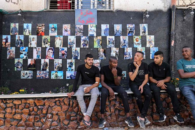 Men sit before a wall displaying pictures of killed Palestinians in Jenin in the north of the occupied West Bank on July 5, 2023, after the Israeli army declared the end of a two-day military operation in the area. (AFP)