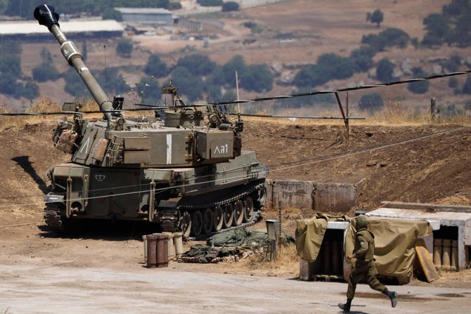 A soldier runs near an Israeli army self propelled artillery vehicle on the outskirts of Kiryat Shmona near Israel's border with Lebanon on July 6, 2023. (AFP)