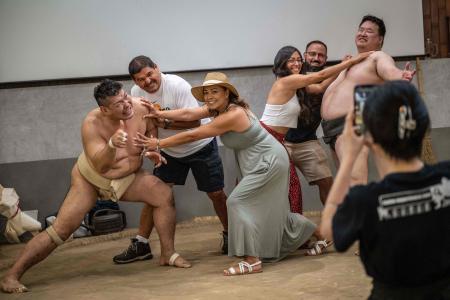 This picture taken on July 3, 2023 shows foreign tourists posing for photographs with former sumo wrestlers at the Yokozuna Tonkatsu Dosukoi Tanaka restaurant in Tokyo. (AFP)