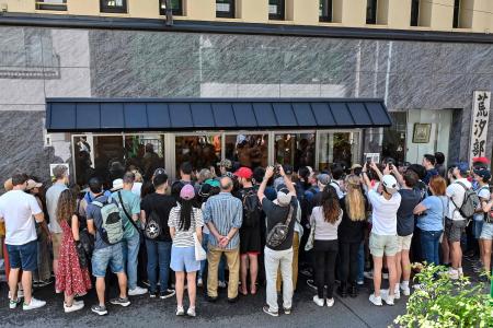 This photo taken on June 7, 2023 shows a group of people, many of them tourists, trying to watch a sumo training session through the glass windows at the Arashio-beya sumo stable in Tokyo. (AFP)