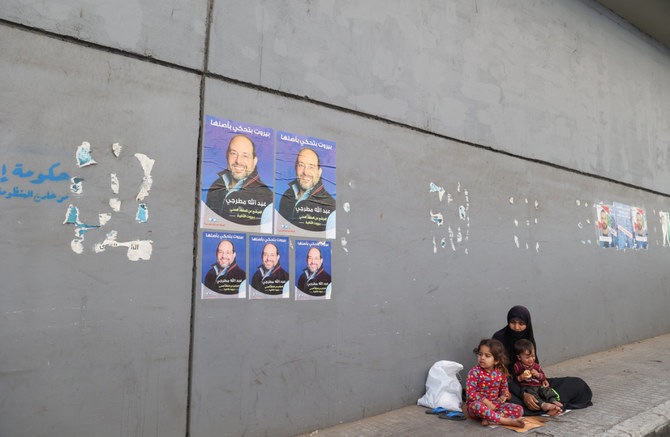 A beggar and her children sit on the sidewalk beneath electoral posters under the Cola bridge in the Lebanese capital Beirut, on April 27, 2022. (AFP)
