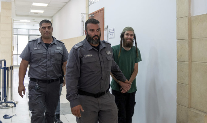 Elisha Yared, 22, right, is led handcuffed by officers during an appearance at the Jerusalem District Court on Tuesday, Aug. 8, 2023. Yared is one of two Israeli settlers arrested on suspicion of involvement in the killing of a Palestinian man in the West Bank on Friday. (AP)