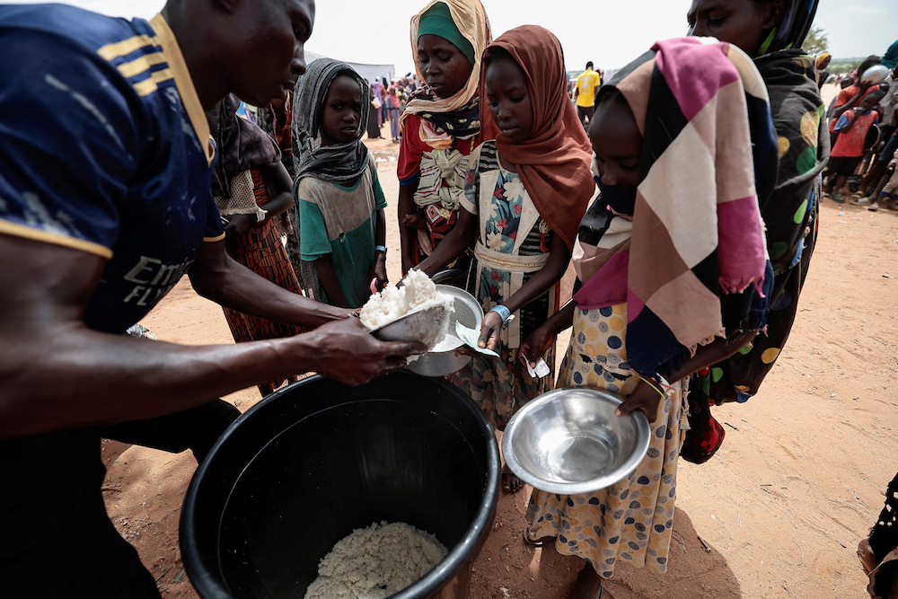 Sudanese girls who fled the conflict in Geneina in Sudan's Darfur region, receive rice portions from Red Cross volunteers in Ourang on the outskirts of Adre, Chad July 25, 2023. (Reuters)