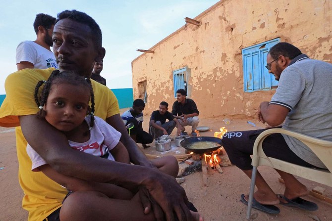 People sit around food cooking on a bonfire at a school that has been transformed into a shelter for people displaced by conflict in Sudan. (AFP)