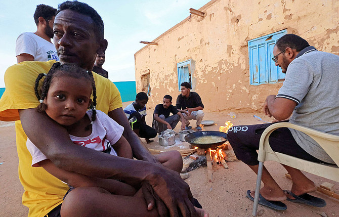 Displaced people sit around food cooking on a bonfire at a school in Sudan’s northern border town of Wadi Halfa. (AFP)