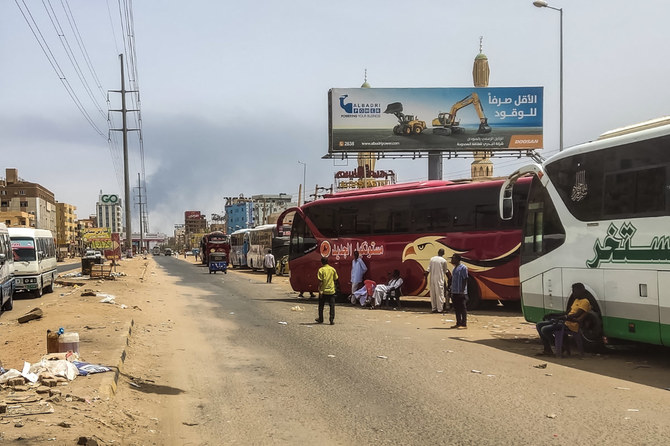 People wait next to passenger buses as smoke billows in an area in Khartoum where fighting between Sudan's army and the paramilitary forces continues to this day. (AFP/File photo)