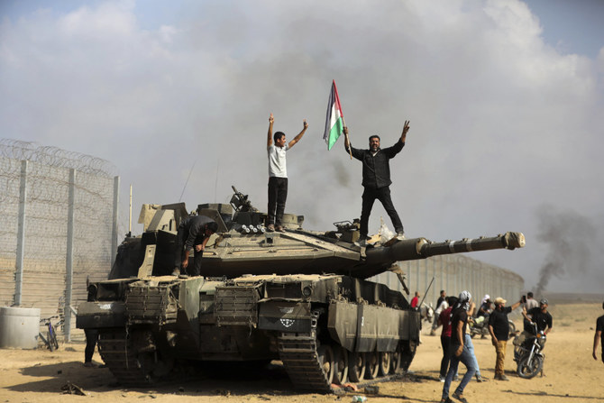 Palestinians wave their national flag and celebrate by a destroyed Israeli tank at the Gaza Strip fence east of Khan Younis on Oct. 7, 2023. (AP Photo)