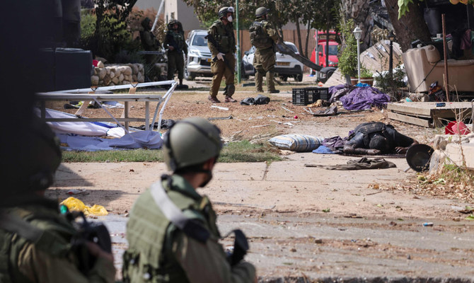 Israeli soldiers stand near the body of a Palestinian militant in Kfar Aza, south of Israel bordering Gaza Strip, on October 10, 2023. (AFP)