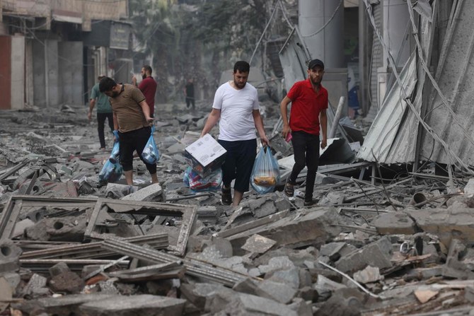 Palestinian men carry food supplies as they walk through debris amid the destruction from Israeli air strikes in Gaza City’s Rimal neighborhood on Oct. 10, 2023. (AFP)