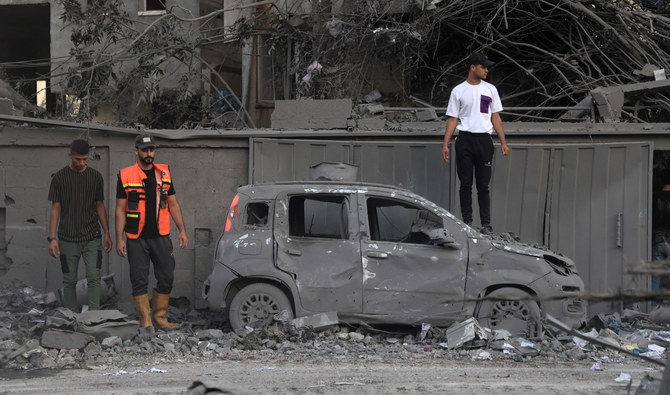 A rescuer and people stand near a burnt car following an Israeli strike in Rafah in the southern Gaza Strip, on October 15, 2023. (AFP)