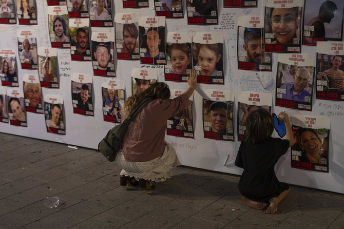 An Israeli woman touches photos of Israelis missing and held captive in Gaza, displayed on a wall in Tel Aviv, on Saturday, Oct. 21, 2023. (AP)