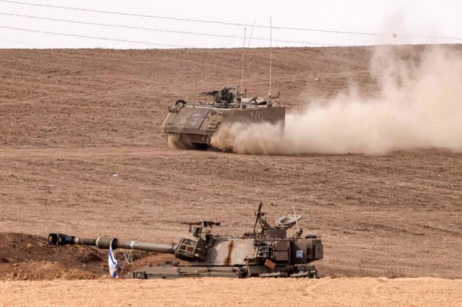 An Israeli army armored tracked vehicle moves near a stationed artillery howitzer at a position along the border with the Gaza Strip in southern Israel on Oct. 31, 2023. (AFP)