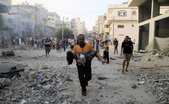 A Palestinian carrying a child runs following an Israeli strike, in Khan Yunis in the southern Gaza Strip on October 14, 2023. (File/AFP)