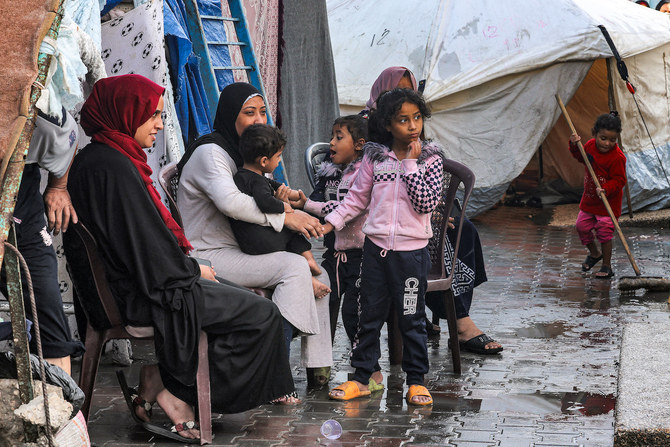 Women sit with children outside tents at a school run by UNRWA. (File/AFP)